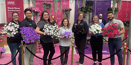 Seven PanAmerican Seed team members hold colourful flowers in front of our Wave Petunias CAST24 display.