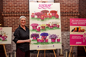 Anne Geddes stands next to a large print on an easel featuring babies in pink pots next to Wave petunias..