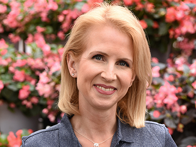 Photo is a closeup headshot of Sarah Makiejus in front of colorful begonias.